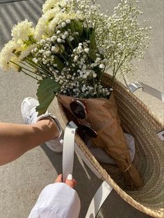 a person holding a brown paper bag with white flowers in it and sunglasses on the handle