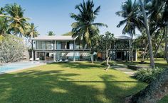 the house is surrounded by palm trees and lawns, with a swimming pool in the foreground