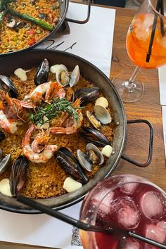 seafood and rice dish served in pans with drinks on the side at a restaurant