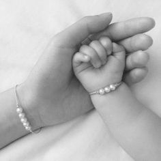 a black and white photo of a baby holding the hand of an adult's hand