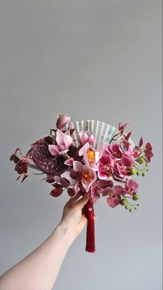 a hand holding a bouquet of flowers with a fan in the middle, on a gray background