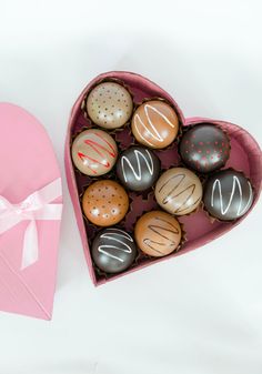 a heart shaped box filled with assorted chocolates next to a pink paper heart