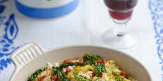 a white bowl filled with vegetables next to a glass of wine on a blue and white table cloth