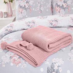 a blanket and two pillows on top of a bed in a room with pink flowers