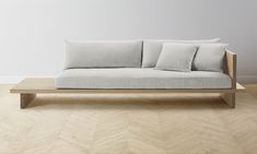 a couch with three pillows on it sitting in front of a white wall and wooden floor