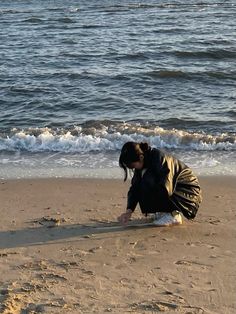 a woman kneeling down on top of a sandy beach