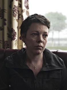 a woman sitting on top of a couch next to a window with curtains behind her