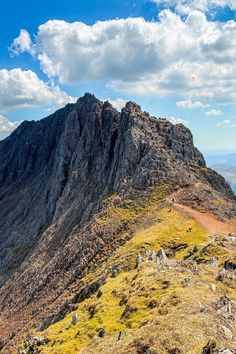 the top of a mountain with grass and rocks on it, under a cloudy blue sky