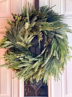 a wreath hanging on the front door of a house decorated with evergreen and pine needles