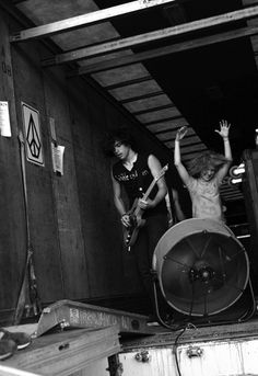 black and white photograph of two people playing guitar in back of truck with roof open