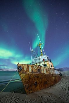 an old rusted boat sitting on top of a sandy beach under the night sky