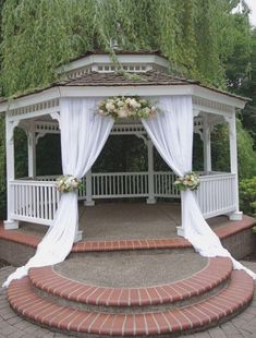 a gazebo with white drapes and flowers on the top is surrounded by brick steps