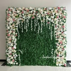 an artificial flower wall with white and pink flowers on the top, surrounded by greenery