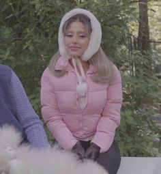 a woman in pink jacket sitting next to a white fluffy animal on top of a table