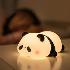 a panda bear lamp sitting on top of a table next to a person sleeping in the background