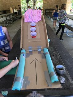 a cardboard box with some cups in it on top of a table and people standing around