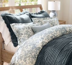 a bed with blue and white comforters in a bedroom next to a window on a wooden headboard