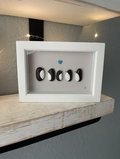 three black and white eggs in a shadow box on a shelf with string lights behind them