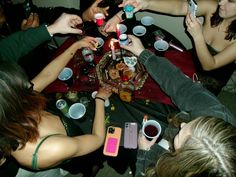 a group of people sitting around a table with cups and candles on it, all holding cell phones