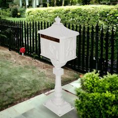 a white mailbox sitting in the middle of a yard next to a fence and shrubbery