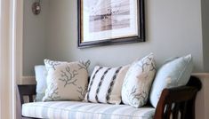 a wooden bench with pillows on it in front of a framed painting and door way