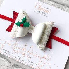 a white bow with red ribbon and holly berry on the side, sitting on top of a piece of paper