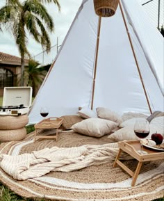 a teepee tent with pillows, blankets and wine glasses on the ground in front of it