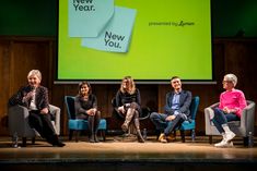 five people sitting on chairs in front of a large screen with new year's written on it