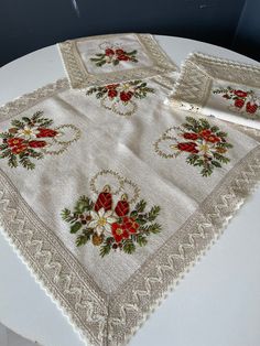 a white table topped with two place mats and napkins covered in red flowers on top of it