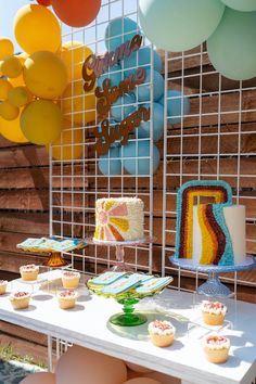 a table topped with cupcakes and cake next to balloons