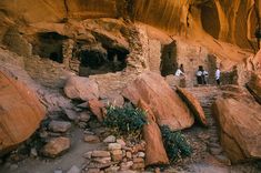 some people are standing in front of some large rocks and rock formations on the side of a mountain