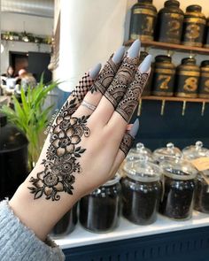 a woman's hand with henna tattoos on it and some jars in the background