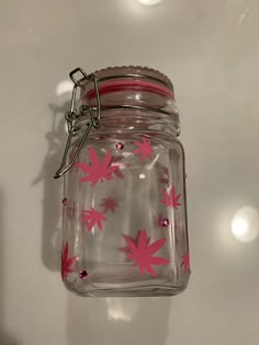 a glass jar with pink flowers on it hanging from a hook in front of a white wall