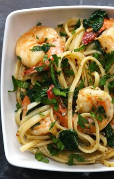 pasta with shrimp, spinach and tomatoes in a white bowl on a black table