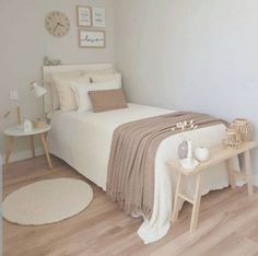 a bedroom with white walls and wood flooring is pictured in this image, the bed has a beige blanket on it