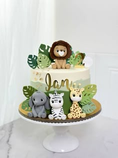 a cake decorated with jungle animals on top of a white tableclothed surface and greenery