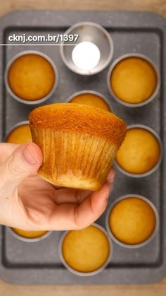 a person holding a muffin in front of a muffin tin filled with cupcakes