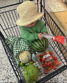 a small child sitting in a shopping cart with fruits and vegetables