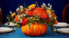 an arrangement of flowers and greenery in a pumpkin shaped centerpiece on a table