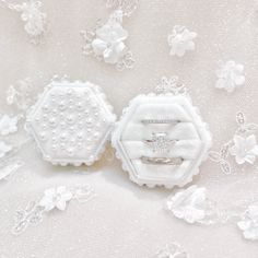 two wedding rings sitting on top of a lace covered table cloth with white flowers and pearls