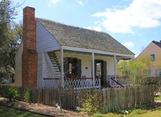 a small white house with a wooden fence around it and a brick chimney in the front yard