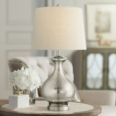 a silver table lamp sitting on top of a wooden table next to a white flower