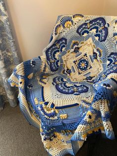 a crocheted blue and yellow blanket sitting on top of a chair next to a window