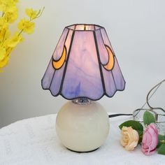 a table lamp sitting on top of a white table next to pink roses and yellow flowers