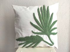 a white pillow with a green leaf design on the front and back, sitting on a shelf