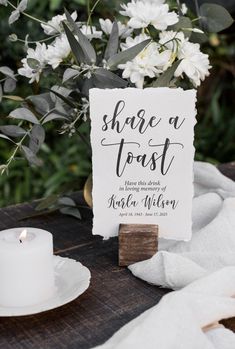 a sign that says share a toast next to a candle and some flowers on a table