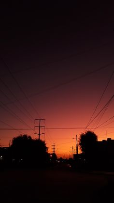 the sun is setting behind power lines and telephone poles in an urban area at dusk