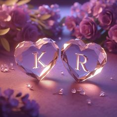 two crystal hearts with the letters k and r in front of them on a table next to purple flowers