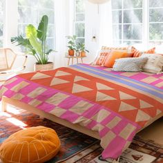 an orange and pink bed in a white room with plants on the windows sill