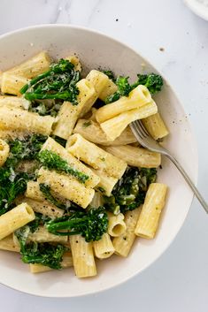 a bowl filled with pasta and broccoli on top of a white countertop